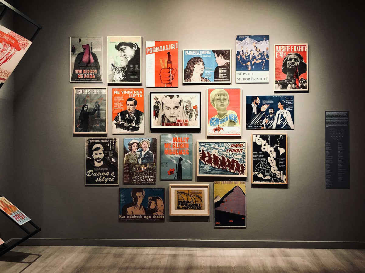 A densely hung wall of colourful prints and posters in a gallery