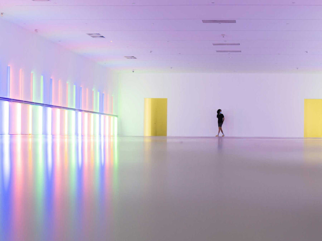 A large-scale coloured light installation filling a museum hall, with a single visitor in the distance