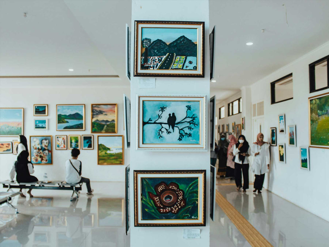 A bright gallery hallway lined with framed paintings of many different kinds