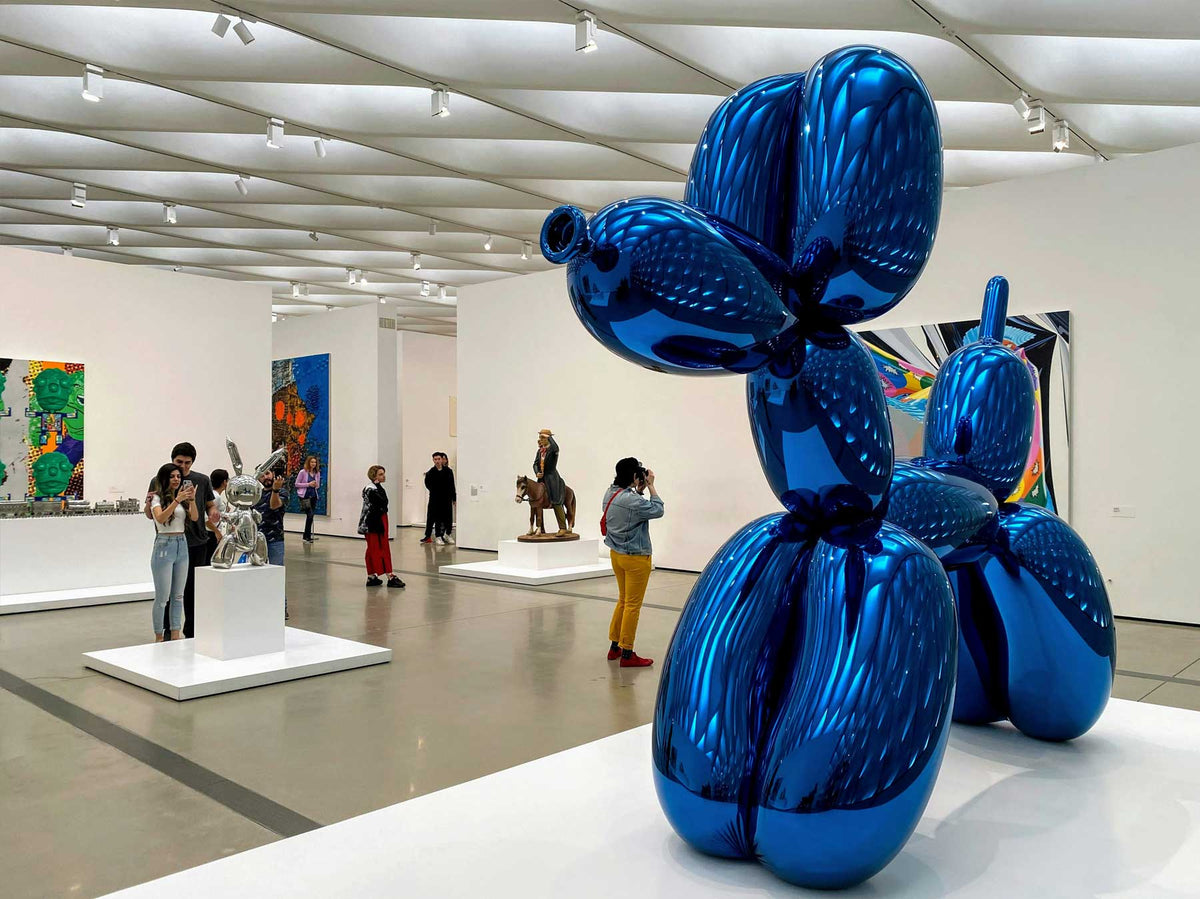 Visitors circulating around a large reflective blue sculpture in a contemporary museum